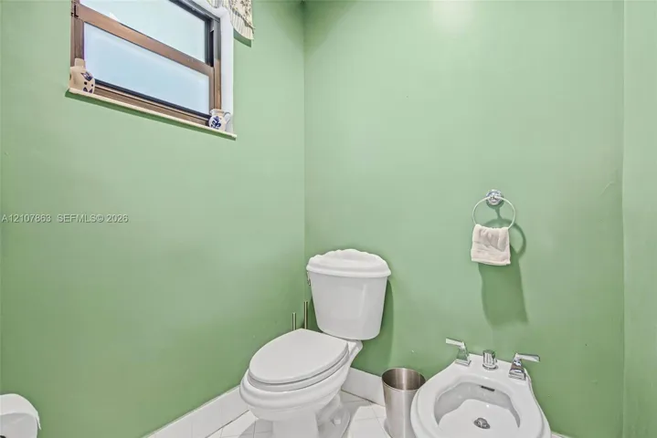 Interior space featuring a white dual-flush toilet, white bidet with chrome faucet, tile flooring, and a window with exterior exposure