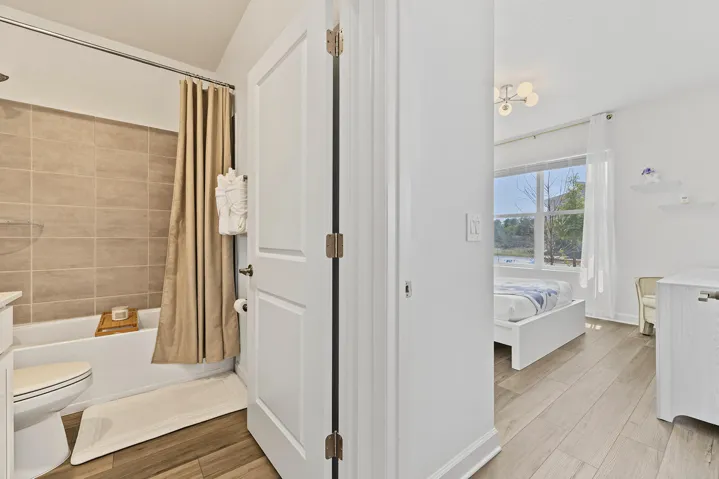 Bathroom featuring a tub-shower combination with horizontal tile surround and vinyl wood-finish flooring, extending into a room with large window and modern overhead lighting