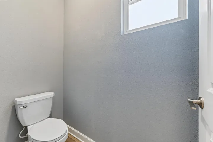 Neutral-toned wall finish, white porcelain toilet, transom window, and brushed metallic hardware.