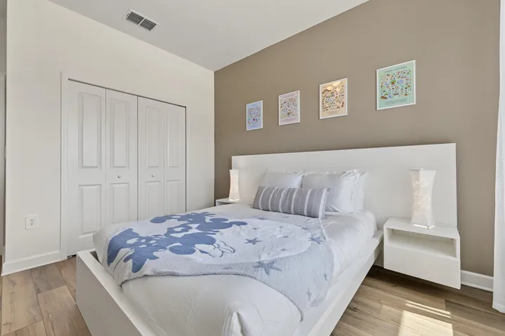 Room featuring vinyl wood-finish flooring, a neutral-toned accent wall, and a built-in white headboard with integrated floating nightstands