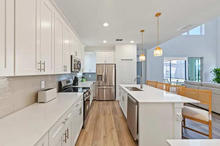 Kitchen featuring white shaker-style cabinetry, quartz countertops, subway tile backsplash, stainless steel appliances, and a central island with an undermount sink and pendant lighting