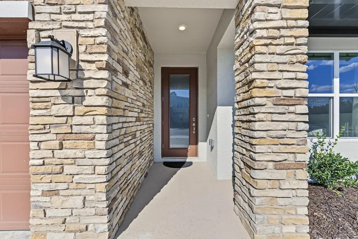 Covered entryway featuring natural stone veneer, a glass-panel entry door, and an exterior wall-mounted carriage light fixture