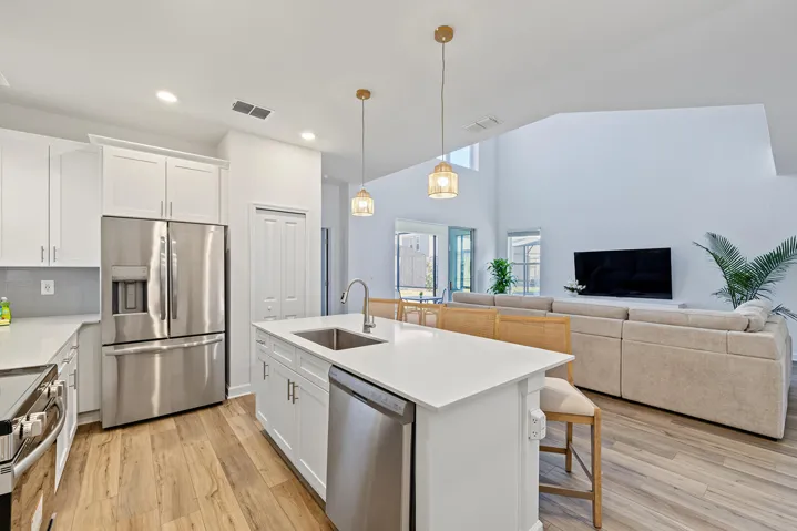 Kitchen featuring a central island with a quartz countertop, stainless steel appliances, white shaker-style cabinetry, pendant lighting, and wood-finish flooring