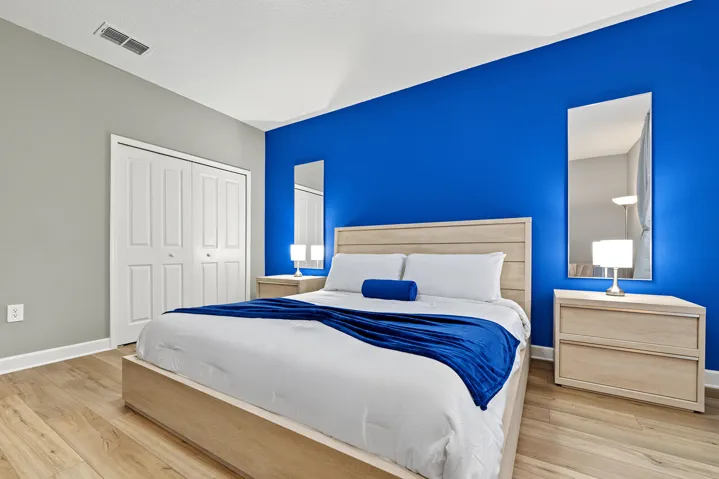 Room featuring vinyl wood-finish flooring, a vaulted ceiling, dual-paneled closet doors, and a contrasting blue accent wall with integrated vertical wall mirrors