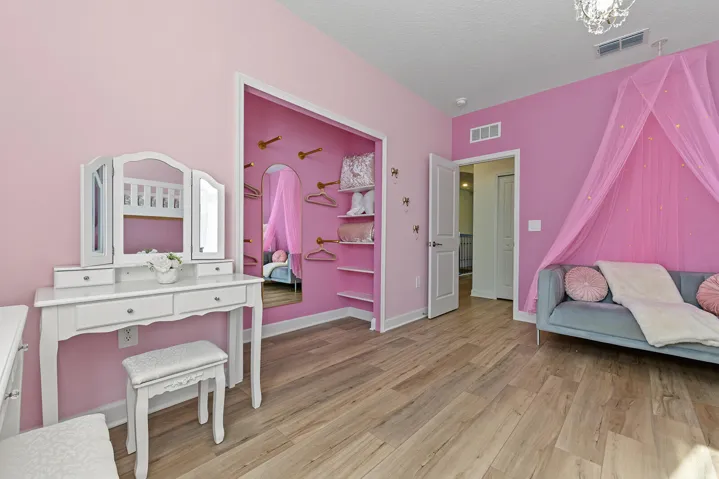 Bedroom featuring vinyl wood-finish flooring, an open-concept closet with custom shelving and wall-mounted hooks, and a multi-panel door