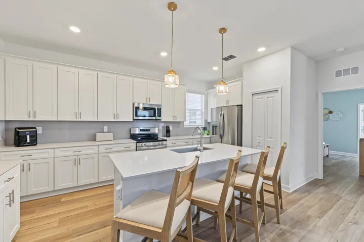 Kitchen featuring white cabinetry, stone-finish countertops, stainless steel appliances, a central island with an integrated sink, and wood-finish flooring