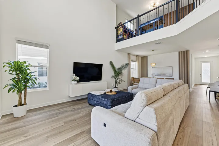 Double-height ceiling, vinyl wood-finish flooring, wall-mounted cabinetry, and a mezzanine level with metal spindle railing
