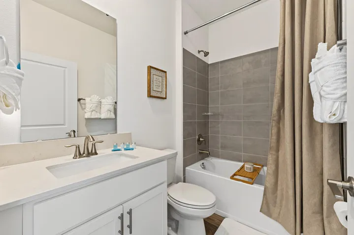 Bathroom featuring a white vanity cabinet, composite countertop with an integrated rectangular sink, wall-mounted mirror, and a tub-shower combination with gray tile surround