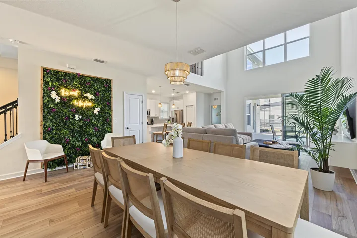 Open-concept living space featuring high ceilings, large windows, vinyl wood-finish flooring, a tiered pendant light fixture, and an integrated decorative wall feature