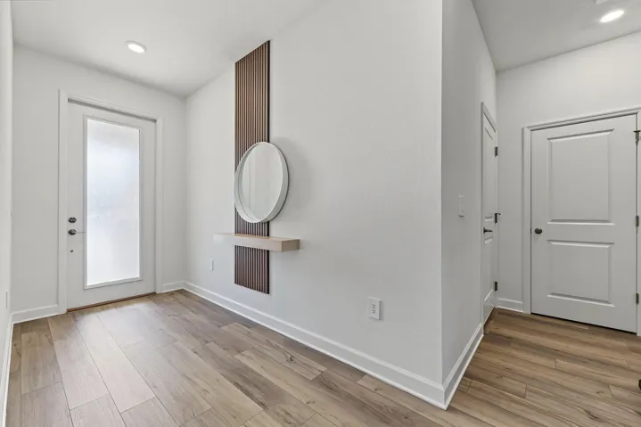 Entryway featuring vinyl wood-finish flooring, a glass-panel front door, and a built-in vertical slat accent wall with a floating shelf