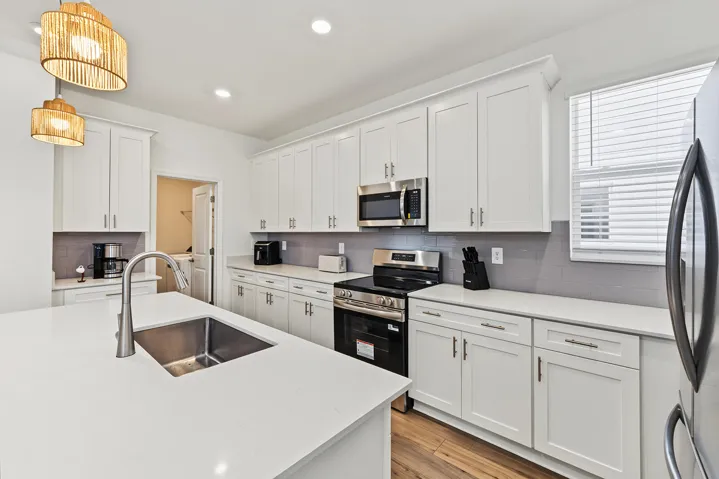 Kitchen featuring white shaker-style cabinetry, quartz countertops, a central island with an undermount sink, stainless steel appliances, and wood-finish flooring