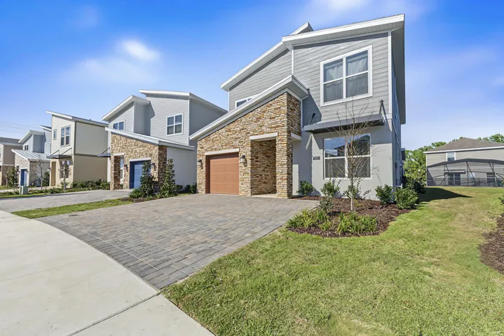 Two-story exterior featuring stone veneer accents, horizontal lap siding, and a paver driveway leading to an attached garage