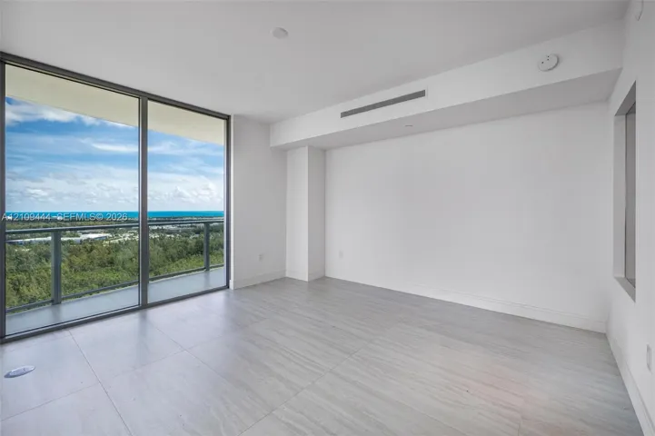 Floor-to-ceiling glass sliding doors, private balcony, neutral large-format tile flooring, and floor-to-ceiling windows with coastal horizon scenery