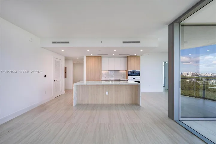 Kitchen featuring an island with stone-finish countertop, wood-finish cabinetry, built-in stainless steel wall oven, recessed lighting, and expansive floor-to-ceiling glass sliding doors