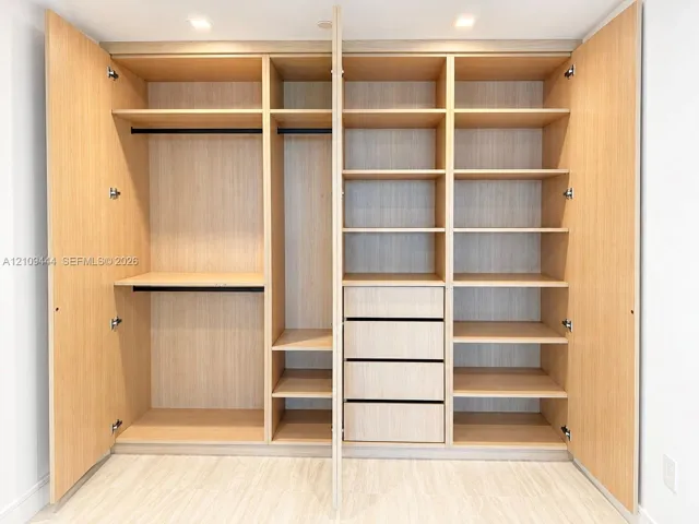 Custom floor-to-ceiling cabinetry with light wood finish, integrated hanging rods, multiple adjustable shelving tiers, and built-in drawer storage