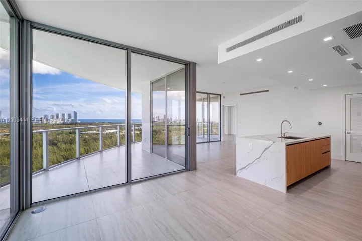 Floor-to-ceiling glass walls, expansive wraparound balcony, kitchen island with waterfall-edge stone countertop, wood-finish cabinetry, and neutral large-format tile flooring