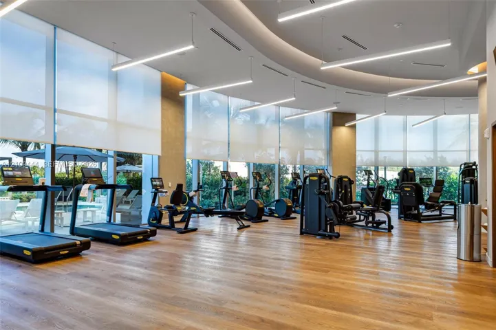 Fitness center featuring floor-to-ceiling windows, wood-finish flooring, curved recessed ceiling architecture, and linear pendant lighting