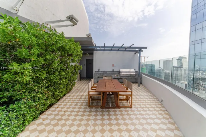 Rooftop terrace featuring patterned tile flooring, a built-in outdoor kitchen with stone countertop, stainless steel grill, pergola structure, and glass panel railing