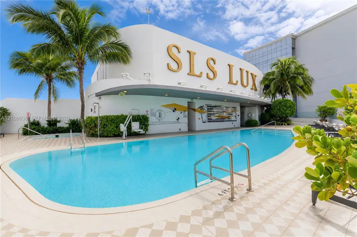 Outdoor swimming pool featuring a curved concrete deck, metallic handrails, built-in wall mural, and mature palm trees