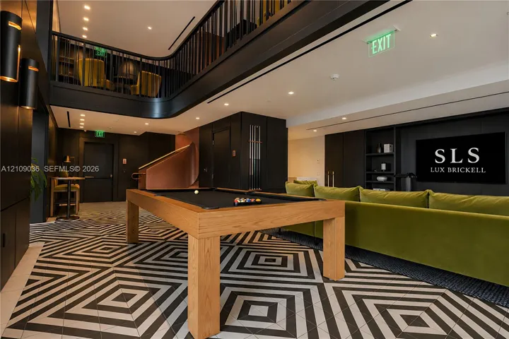 Geometric patterned tile flooring, double-height ceiling with mezzanine balcony, black metal railings, recessed lighting, and built-in wall cabinetry