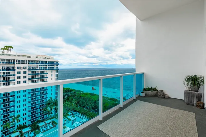 Private balcony featuring a glass-panel railing and concrete flooring, showcasing an expansive ocean and coastal panorama