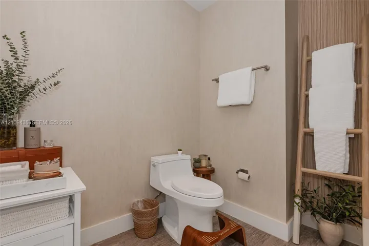 Neutral-toned wallpaper, white one-piece toilet, wood-finish flooring, and vertical wood-slat accent paneling