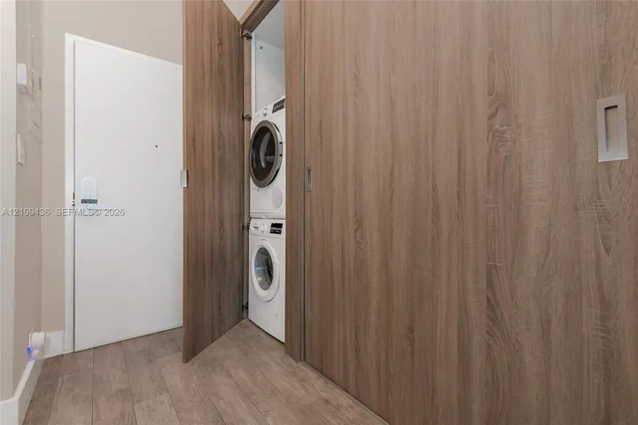 Laundry closet featuring a stackable washer and dryer unit, wood-finish cabinetry, and sliding door paneling