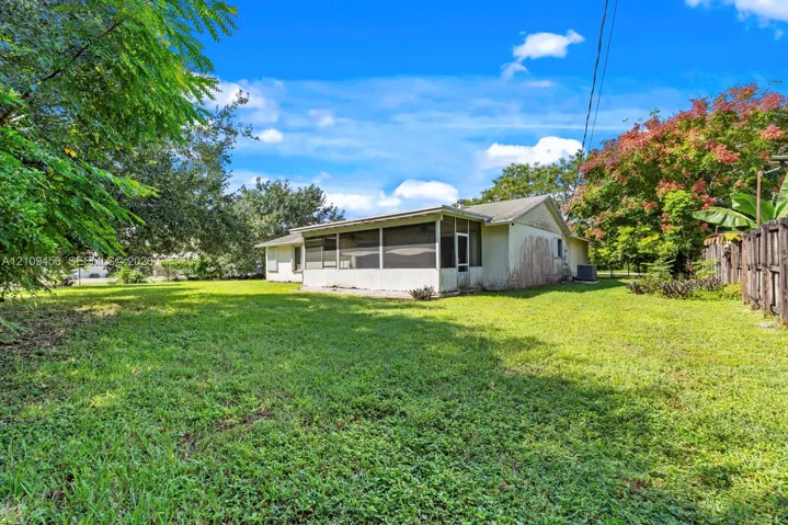 Expansive backyard featuring a large grass lawn, mature trees, and a screened-in porch with a gabled roofline