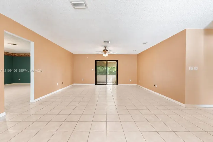 Open-concept interior featuring light-toned tile flooring, neutral wall paint, a ceiling-mounted light fixture with fan, and black-framed sliding glass doors