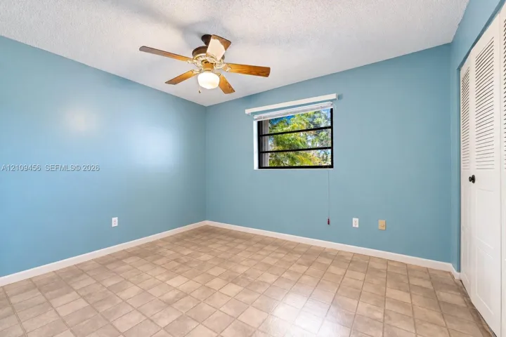 Room featuring ceramic tile flooring, a multi-blade ceiling fan with integrated lighting, and a closet with louvered bi-fold doors