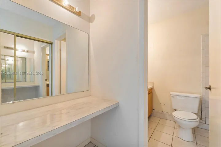 Full-width wall mirror, wood-finish countertop, tiled flooring, and porcelain toilet