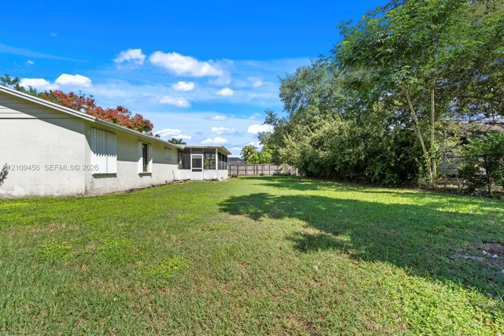 Backyard featuring a grass lawn, screen-enclosed patio, stucco exterior, mature trees, and perimeter fencing