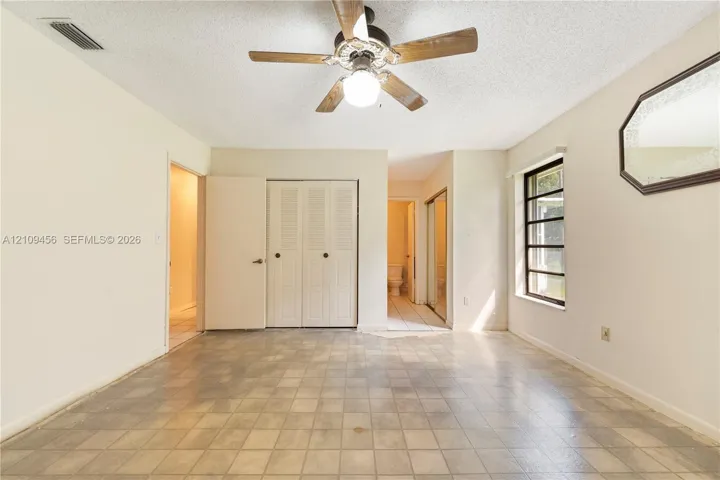 Room featuring square tile flooring, a multi-pane window, dual-panel closet doors, and a ceiling-mounted fan with integrated lighting