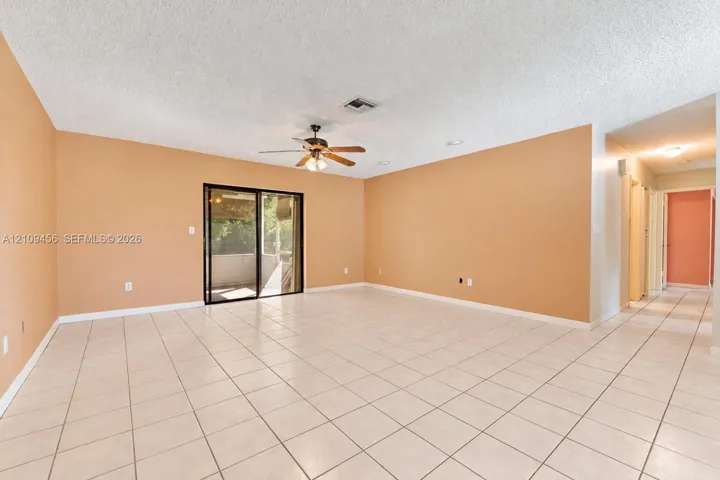 Spacious interior featuring light-toned tile flooring, recessed lighting, ceiling fan with integrated light fixture, and large sliding glass doors