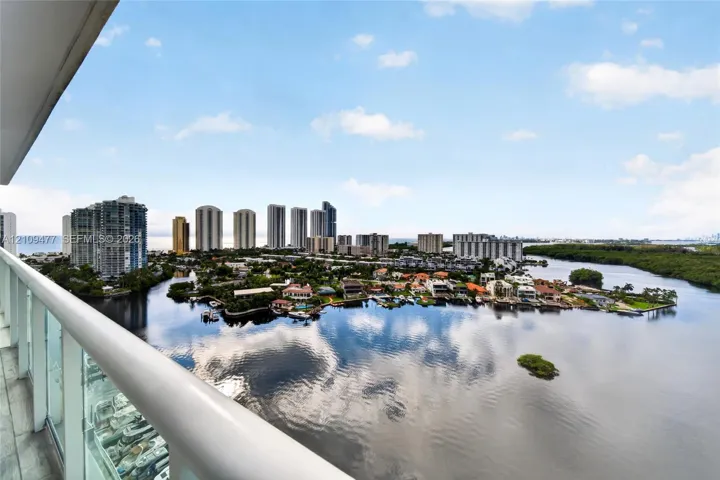 Elevated balcony featuring a glass panel railing, tile flooring, and expansive water, cityscape, and coastal scenery