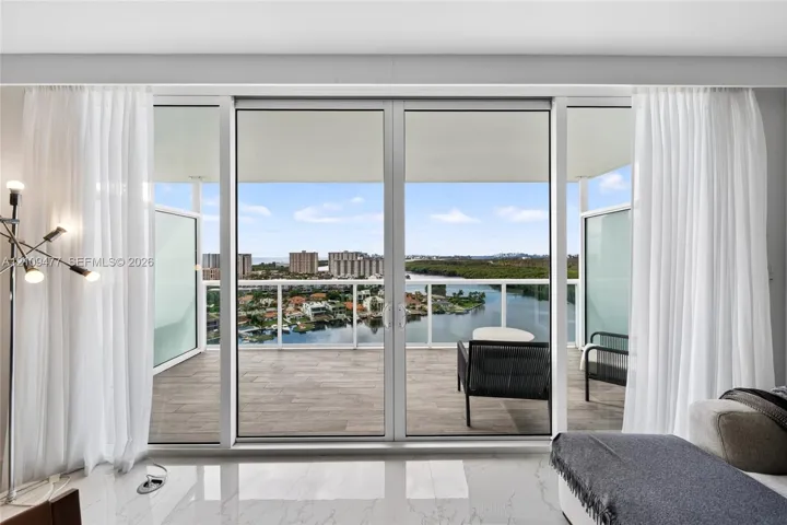 Floor-to-ceiling glass sliding doors opening to a covered balcony with wood-finish decking and metal railings, featuring polished tile flooring