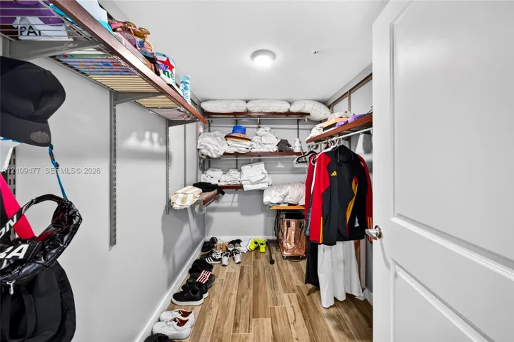 Walk-in storage space featuring wood-finish flooring, adjustable metal shelving, and a flush-mount ceiling light fixture