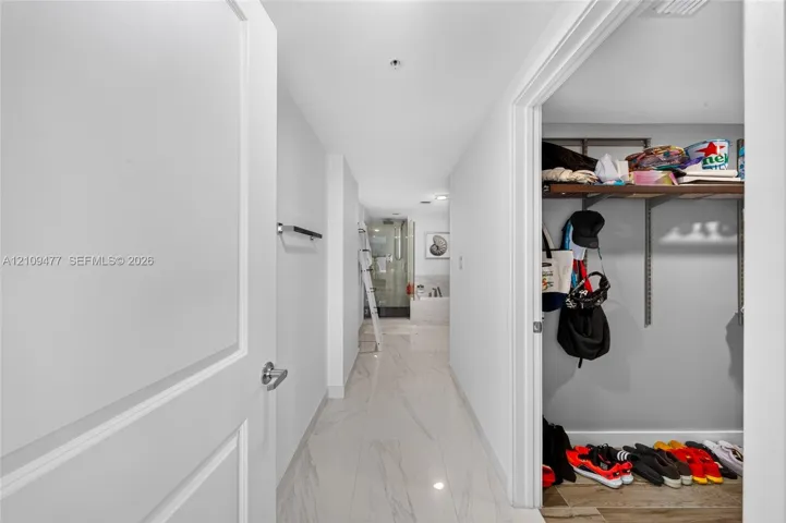 Hallway featuring large-format tile flooring, a wall-mounted metal towel bar, and a walk-in closet with adjustable wire shelving