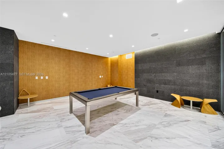 Large room featuring natural stone flooring, textured wood-panel walls, and dark stacked-stone accent wall cladding with recessed ceiling lighting