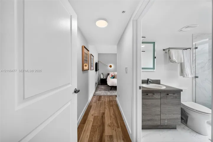 Wood-finish flooring, vanity with stone-style countertop and integrated sink, glass-enclosed shower, and illuminated mirror