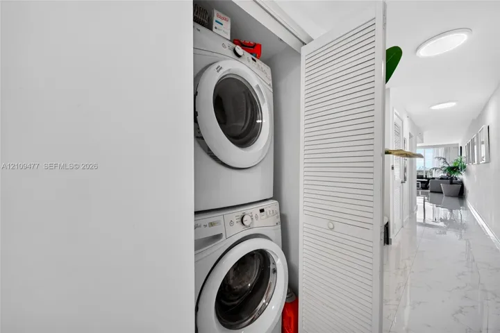 Stacked laundry closet featuring louvered bifold doors and large-format polished tile flooring