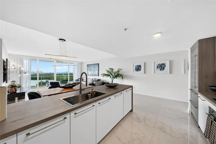 Kitchen featuring white cabinetry, wood-finish countertops, stainless steel undermount sink with high-arc faucet, and large-format tile flooring