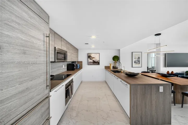 Modern kitchen featuring custom wood-finish cabinetry, sleek white lower cabinetry, integrated stainless steel appliances, and a waterfall-edge island with wood-finish surfacing