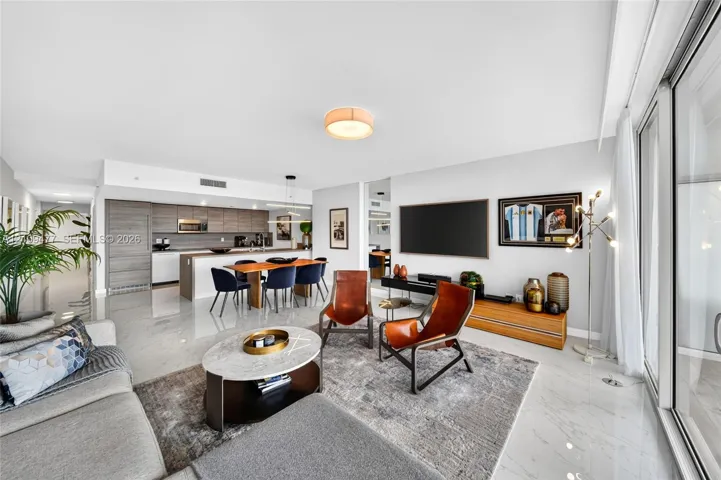 Open-concept living space featuring high-gloss tile flooring, floor-to-ceiling glass sliding doors, and a kitchen equipped with built-in cabinetry and a stone-topped island