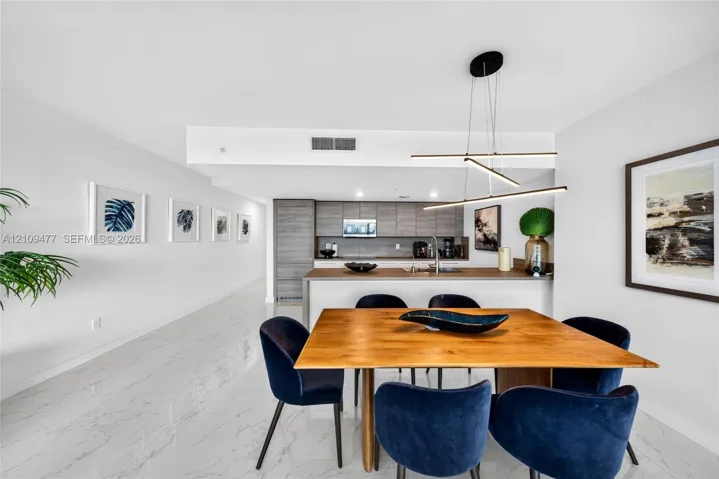 Kitchen featuring flat-panel cabinetry, light-toned countertop, and integrated stainless steel appliances, accented by a linear pendant light fixture and marble-patterned flooring