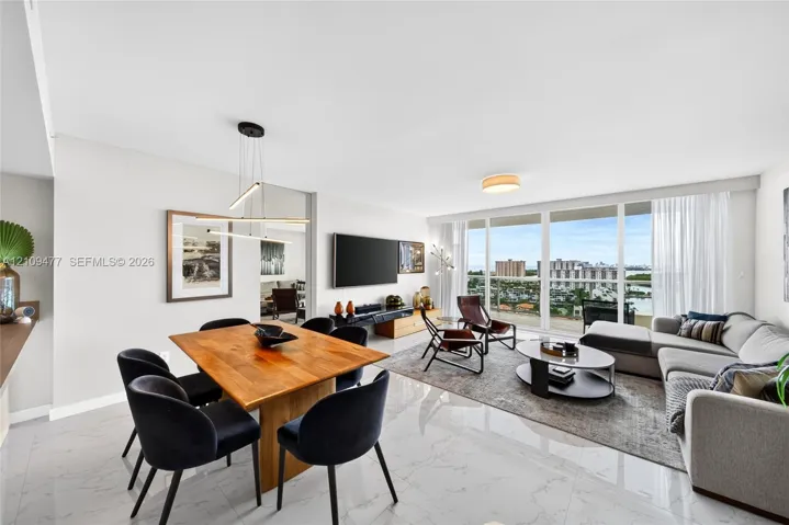 Open-concept interior featuring large-format polished tile flooring, floor-to-ceiling glass panels, a private exterior balcony, and contemporary linear pendant lighting