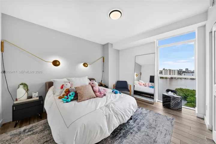 Wood-finish flooring, floor-to-ceiling windows with water and skyline scenery, and dual adjustable metallic wall-mounted sconces
