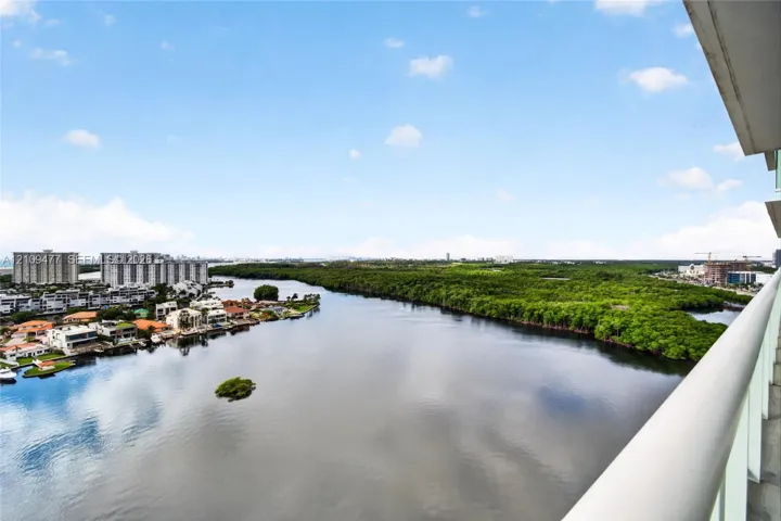 Private balcony with glass panel railing overlooking a waterway, mature mangroves, and residential surroundings
