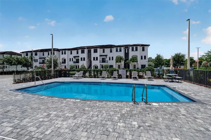 Rectangular swimming pool featuring integrated steps and a paved stone deck, enclosed by perimeter metal fencing