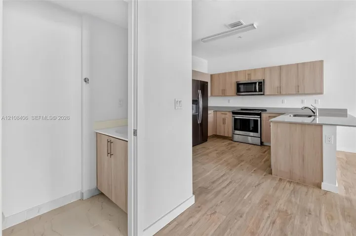 Kitchen featuring light-finish cabinetry, stainless steel appliances, and a peninsula with a stone-surface countertop, complemented by wood-finish flooring throughout